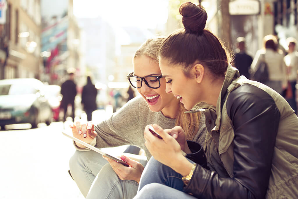 Two young women using a digital tablet to see how they save money on dental treatments.