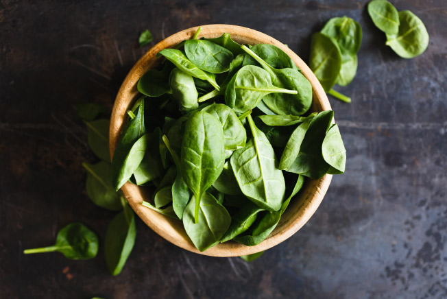 Aerial view of a pile of green spinach in a brown wooden bowl on a gray counter