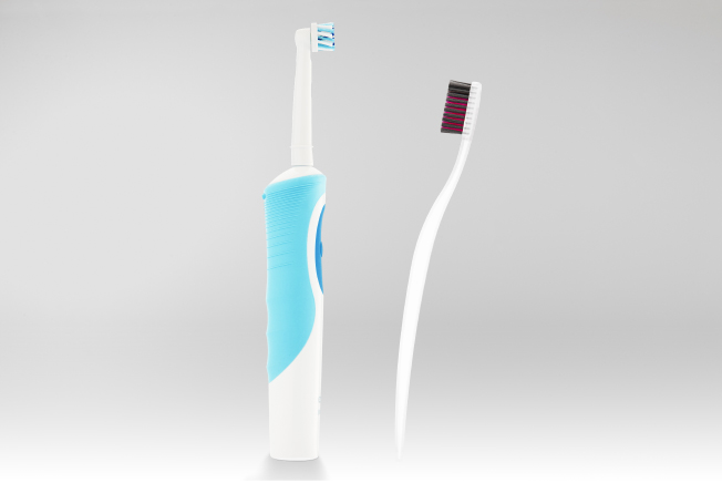 A white and blue electric toothbrush faces a regular toothbrush with a white handle and black and red bristles