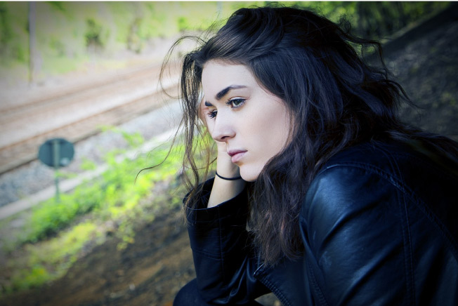 dark haired girl in a black jacket sitting outside worrying about dental anxiety