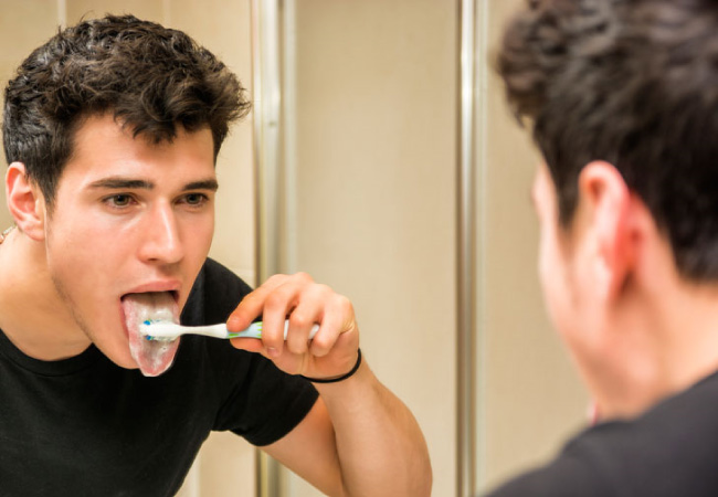 man looking in the mirror brushing his tongue