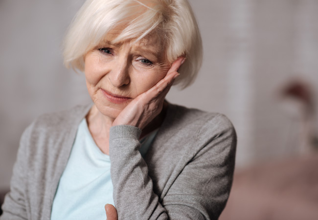 older woman holding her jaw in pain from tmj dysfunction