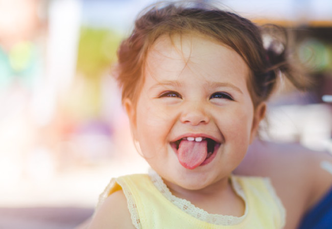 baby girl grins and sticks out her tongue showing off two baby teeth