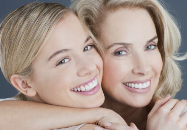 two attractive blond women smile to show off their white teeth