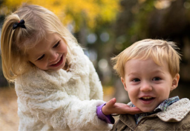 young girl holds her baby brothers chin to show off his smile