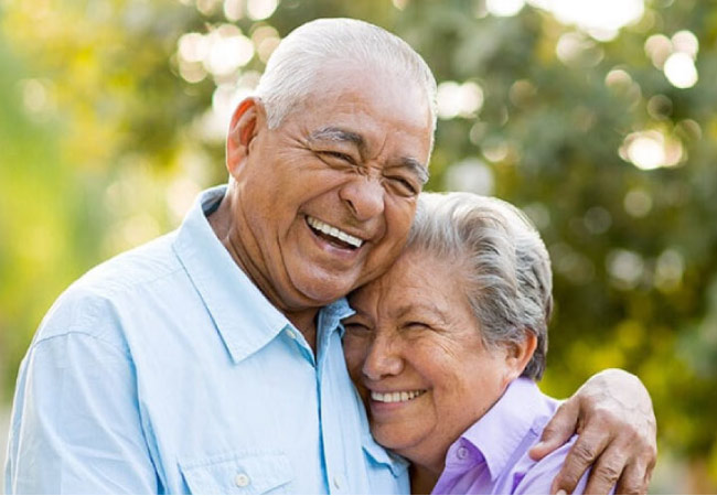 senior couple hug and smile after learning about the benefits of dentures and dental implants