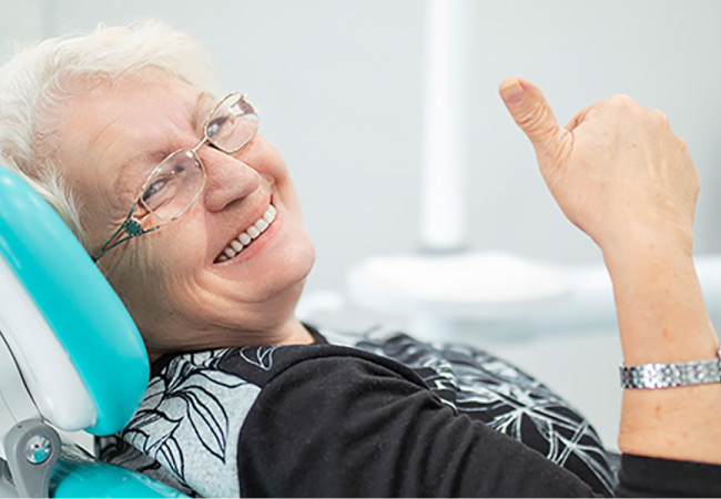 senior woman gives a thumbs up sitting in the dentist's chair