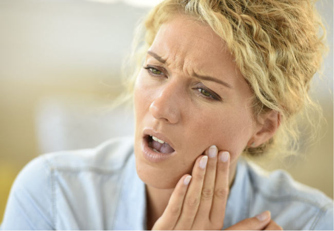 blond woman holds her jaw in pain with TMD