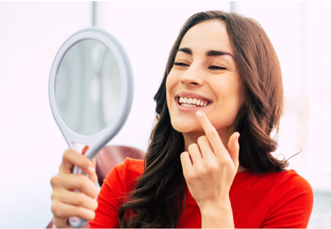 woman holds a mirror and inspects her gums for signs of receeding