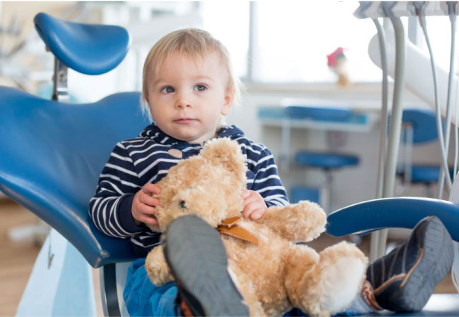 young boy holding a teddy bear sits in the dentist chair 