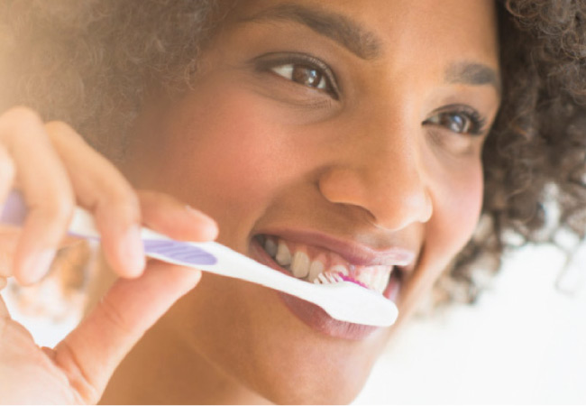 young woman smiles as she brushes her teeth